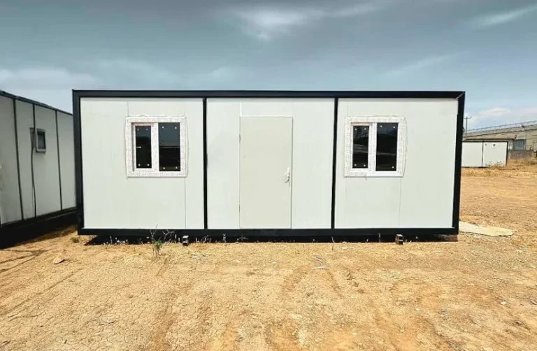 Bürocontainer mit mittiger Tür und zwei Fenstern, Frontansicht auf dem Gelände.
